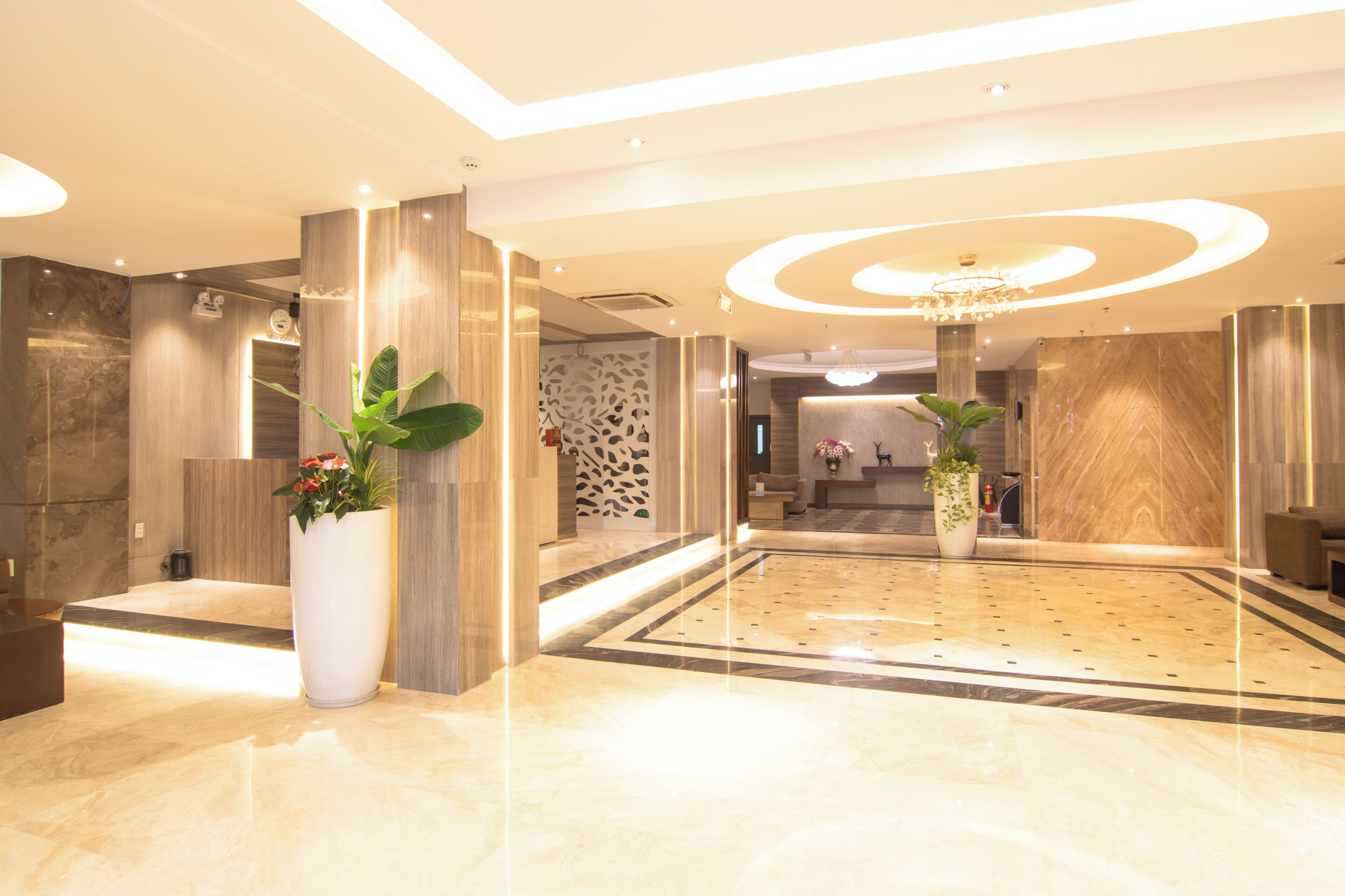 A modern lobby with marble flooring, large potted plants, and a chandelier.