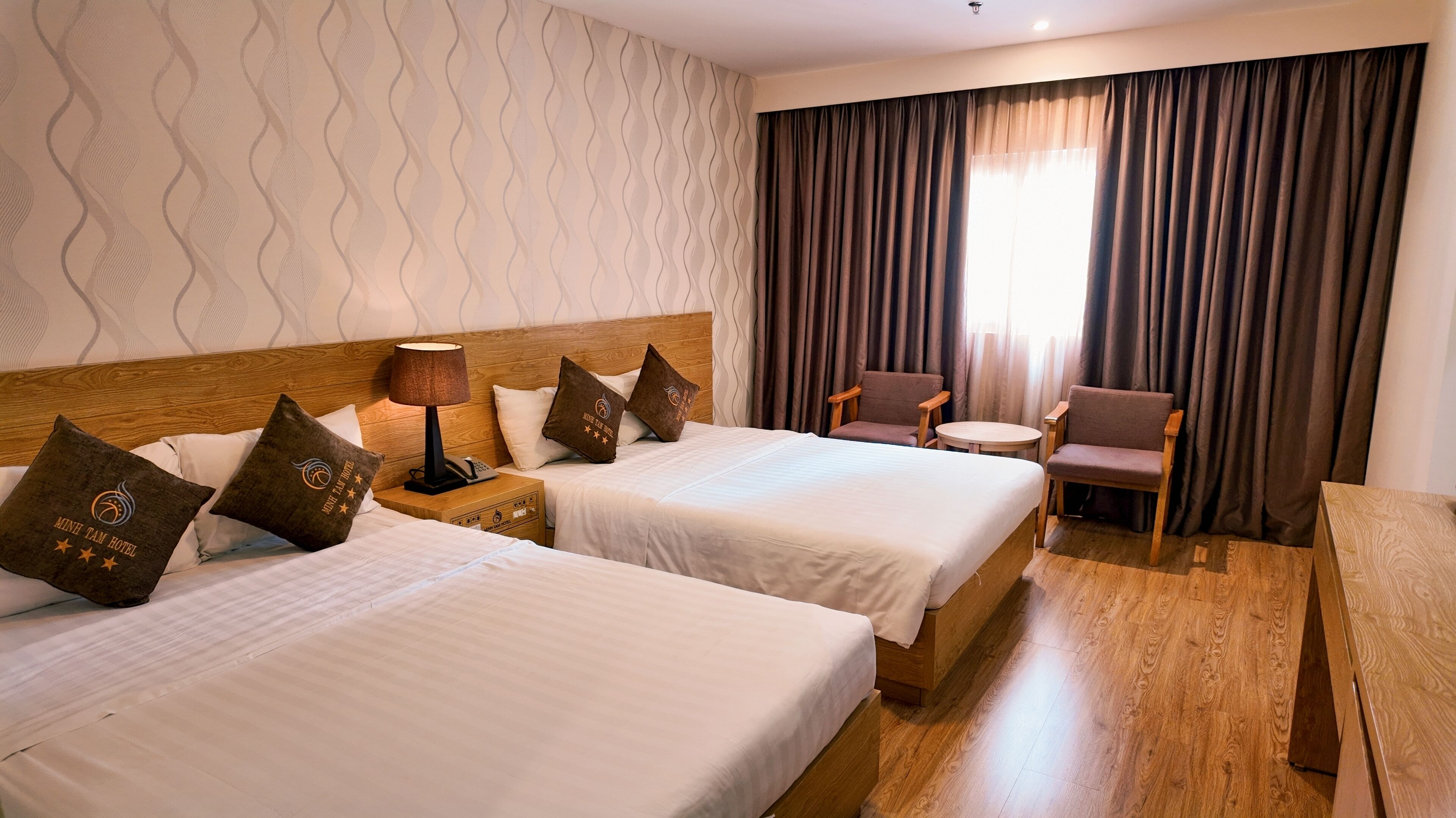 Ein Hotelzimmer mit zwei Betten, einem Nachttisch mit Lampe, einem Sessel und einem kleinen Tisch.