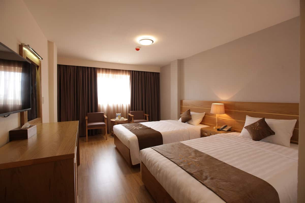 A hotel room with two beds, a desk, a chair, a TV, and a window with curtains.