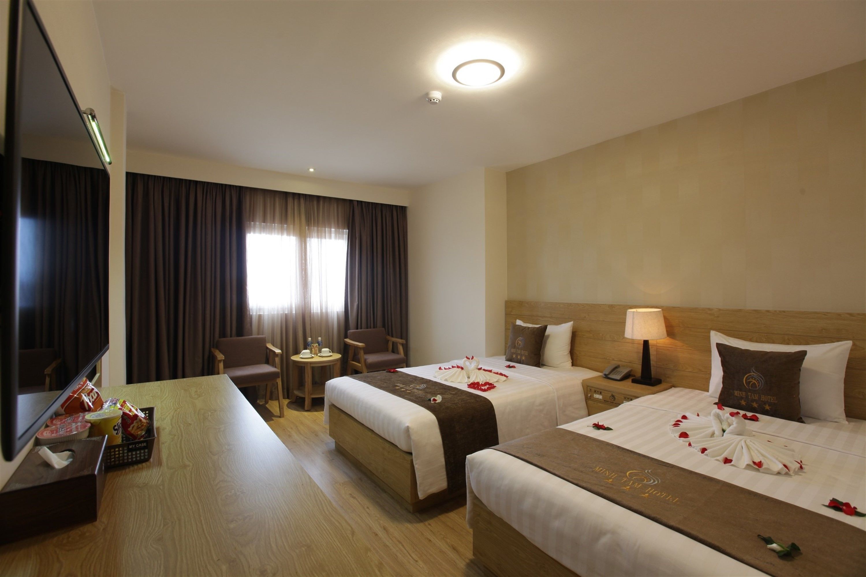 Ein Hotelzimmer mit zwei Betten, einem Schreibtisch, einem Fernseher und einem kleinen Tisch mit einem Stuhl.