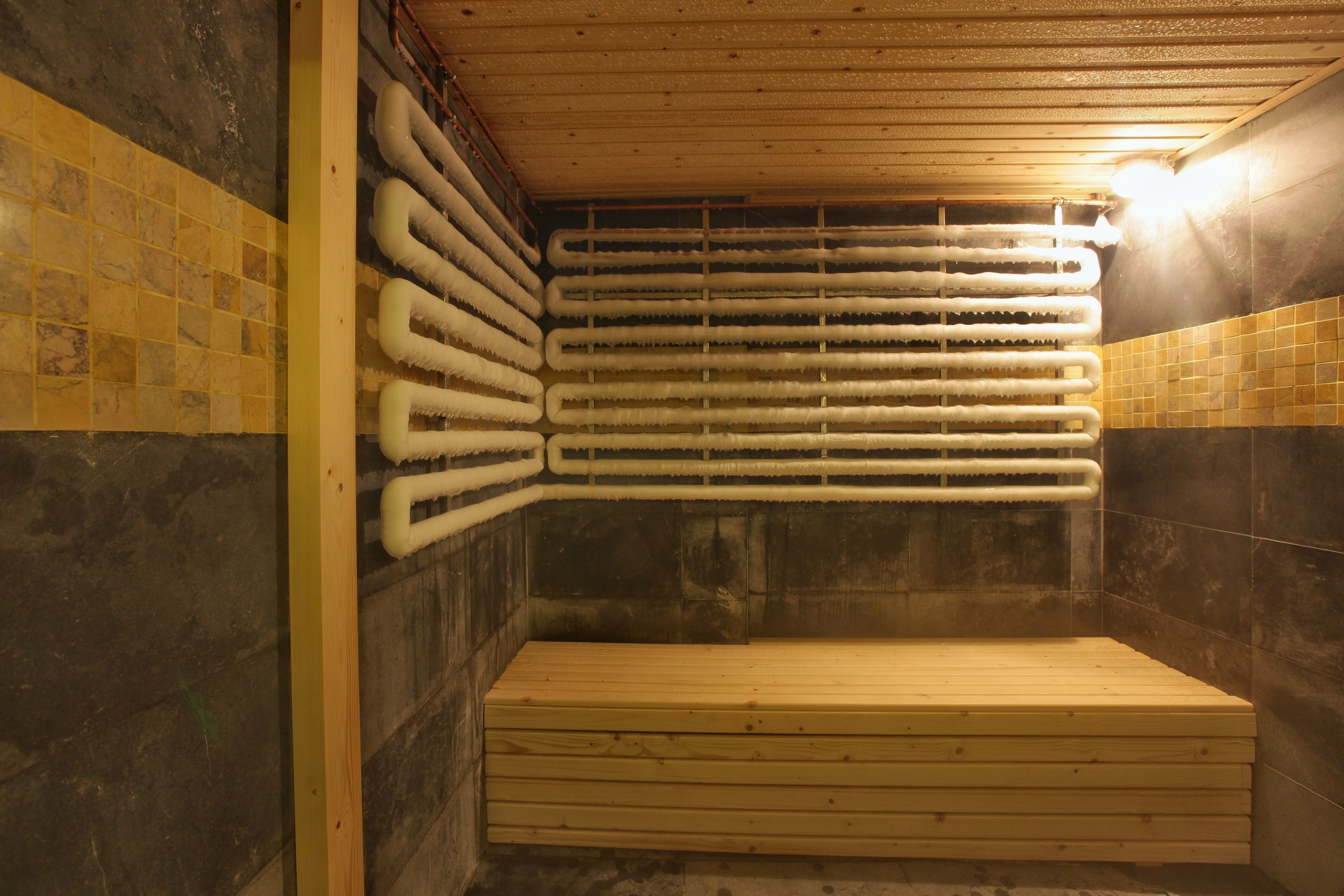 A sauna with a wooden bench, tiled walls, and a ceiling with visible pipes.