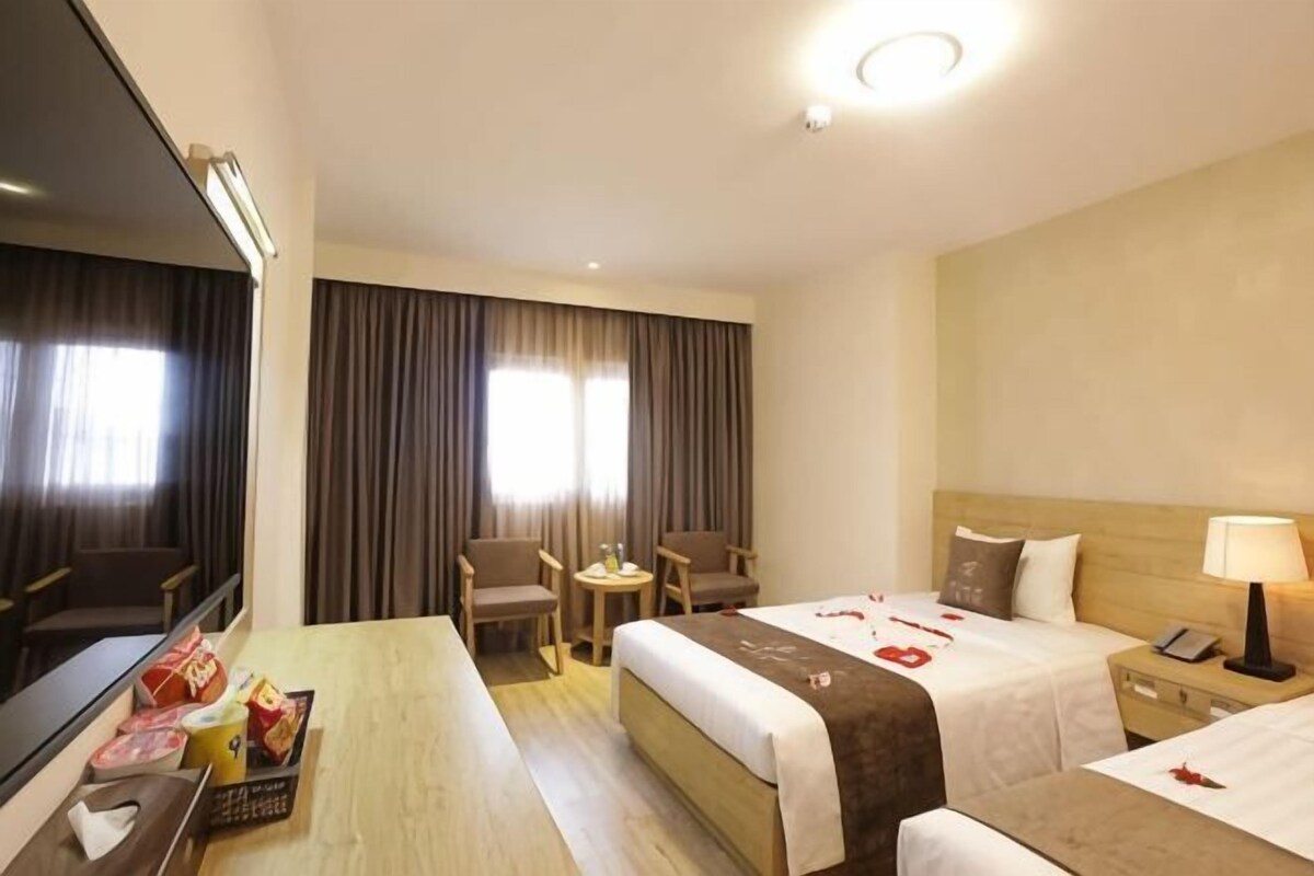 Habitación de hotel con cama, mesitas de noche, escritorio, silla, espejo y ventana con cortinas.