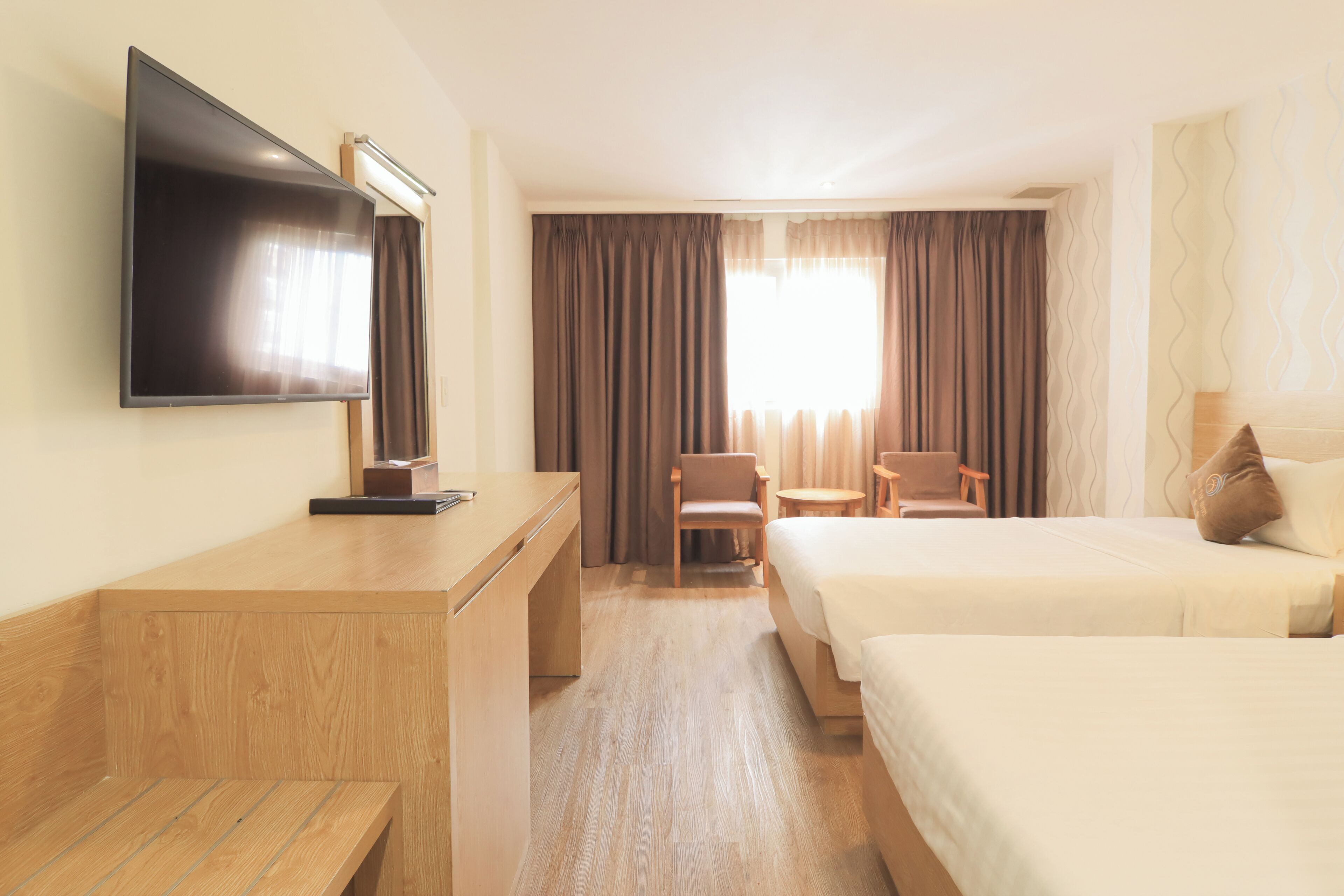 Une chambre d’hôtel équipée d’un téléviseur à écran plat, d’un bureau, de deux lits, d’une chaise, d’une petite table et d’une fenêtre avec des rideaux.