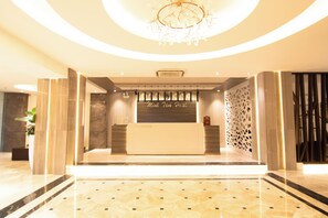Zona de recepción de un hotel con mostrador, candelabro y pared con diseño.