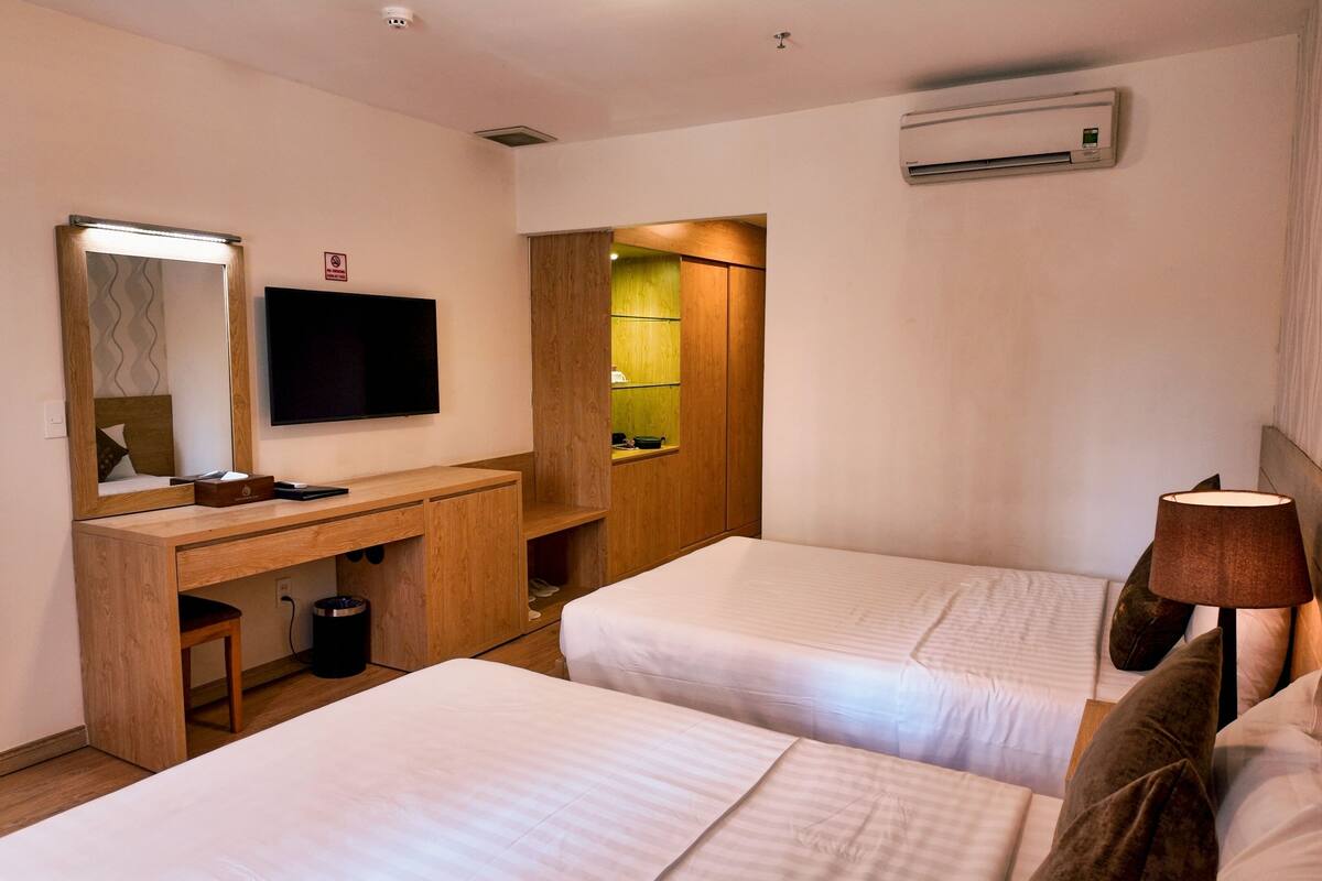 A hotel room with two beds, a desk with a mirror, a TV, an air conditioner, and a lamp.