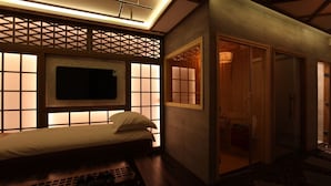 Ein traditioneller japanischer Raum mit Tatami-Bodenbelag, einem niedrigen Holzbett, einer Schiebetür und einem an der Wand montierten Fernseher.