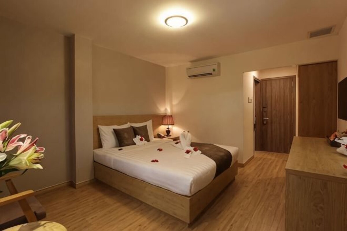 Habitación de hotel con cama, mesita de noche, lámpara y suelo de madera.