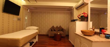 Una habitación compacta con cama, sofá, una mesita redonda, tocador con espejo y televisor montado en la pared.