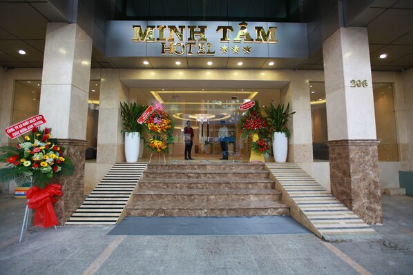 La entrada del Hotel Minh Tam con una escalera que conduce a la entrada, plantas grandes en macetas y un cartel que anuncia una oferta especial.