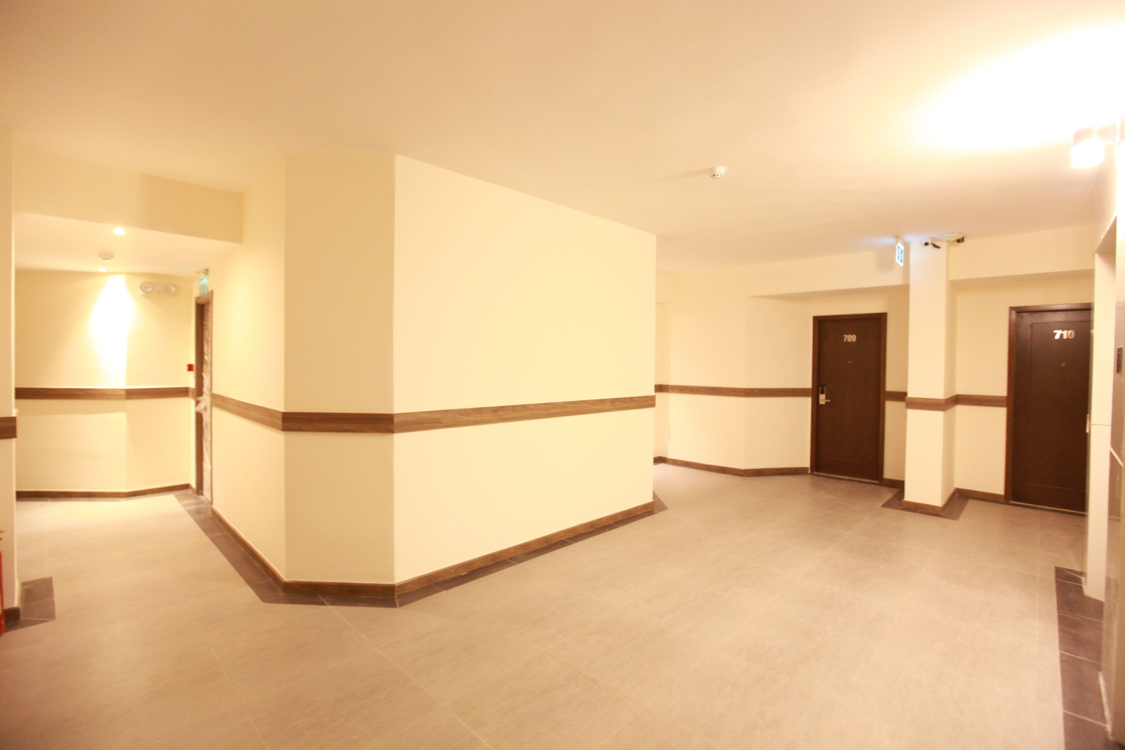 A hotel corridor with beige walls, brown trim, and a tiled floor. There are doors labeled 709 and 710, and a light fixture on the ceiling.