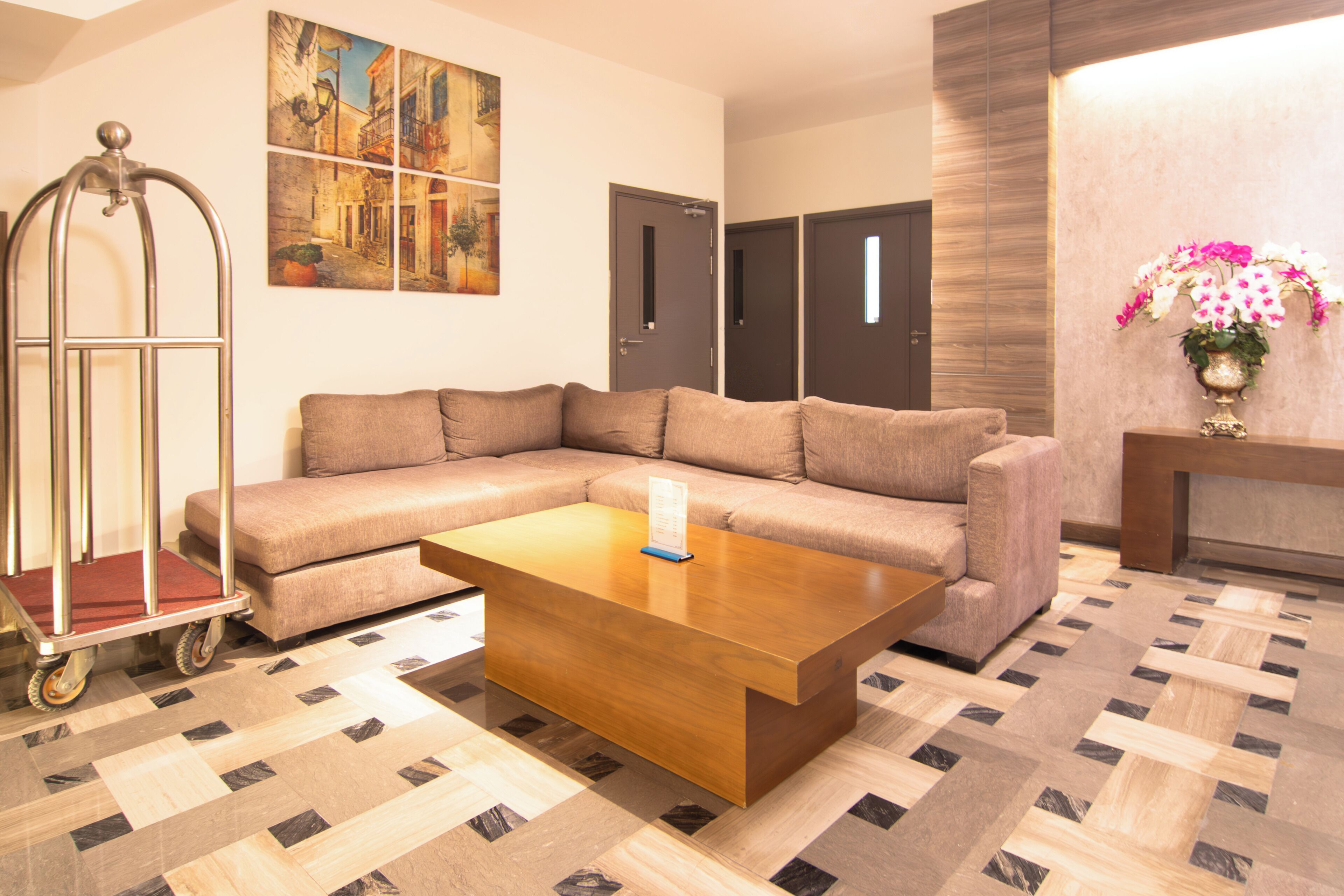 A modern living room with a sectional sofa, a wooden coffee table, a metal cart, and a wall-mounted artwork.