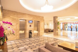 Vestíbulo de hotel con pared de mármol, un ascensor, un mostrador de recepción y una zona de estar.