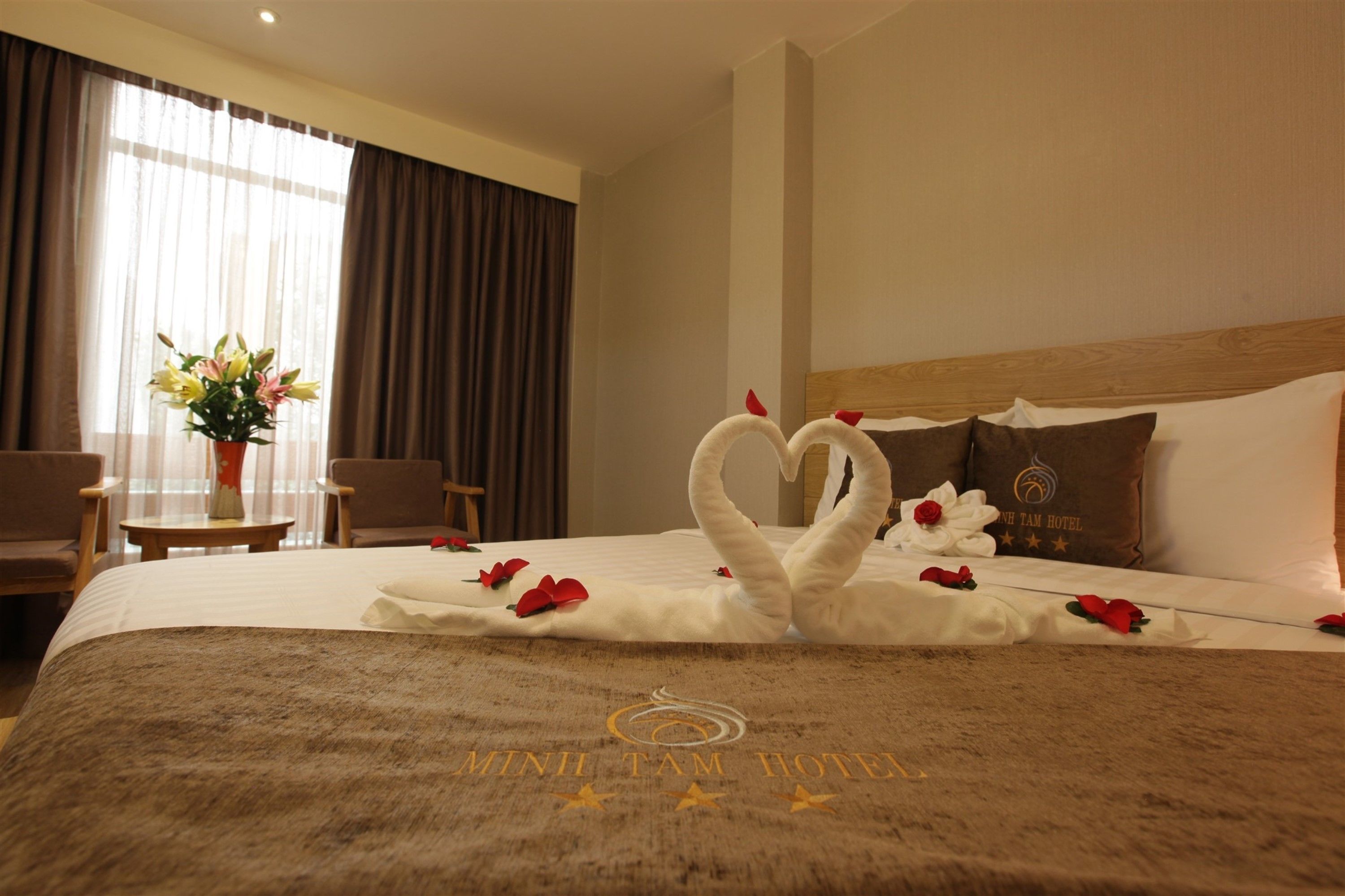 A hotel room with a bed, a headboard, a table with a vase of flowers, and a chair.