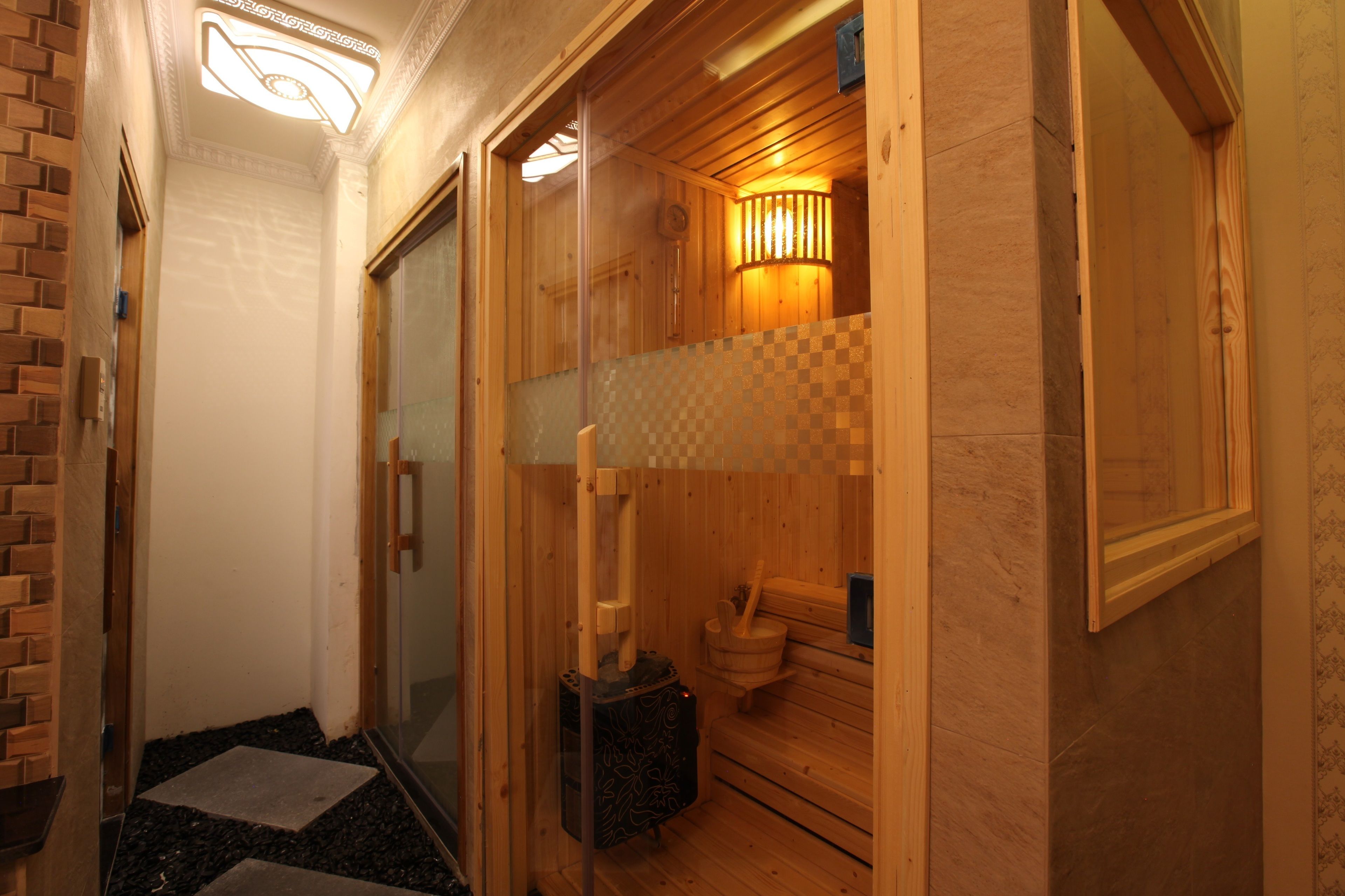 Una sala de sauna con paredes de madera, un banco de madera, suelo de piedra y un calentador fijado a la pared.