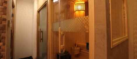 Una sala de sauna con paredes de madera, un banco de madera, suelo de piedra y un calentador fijado a la pared.