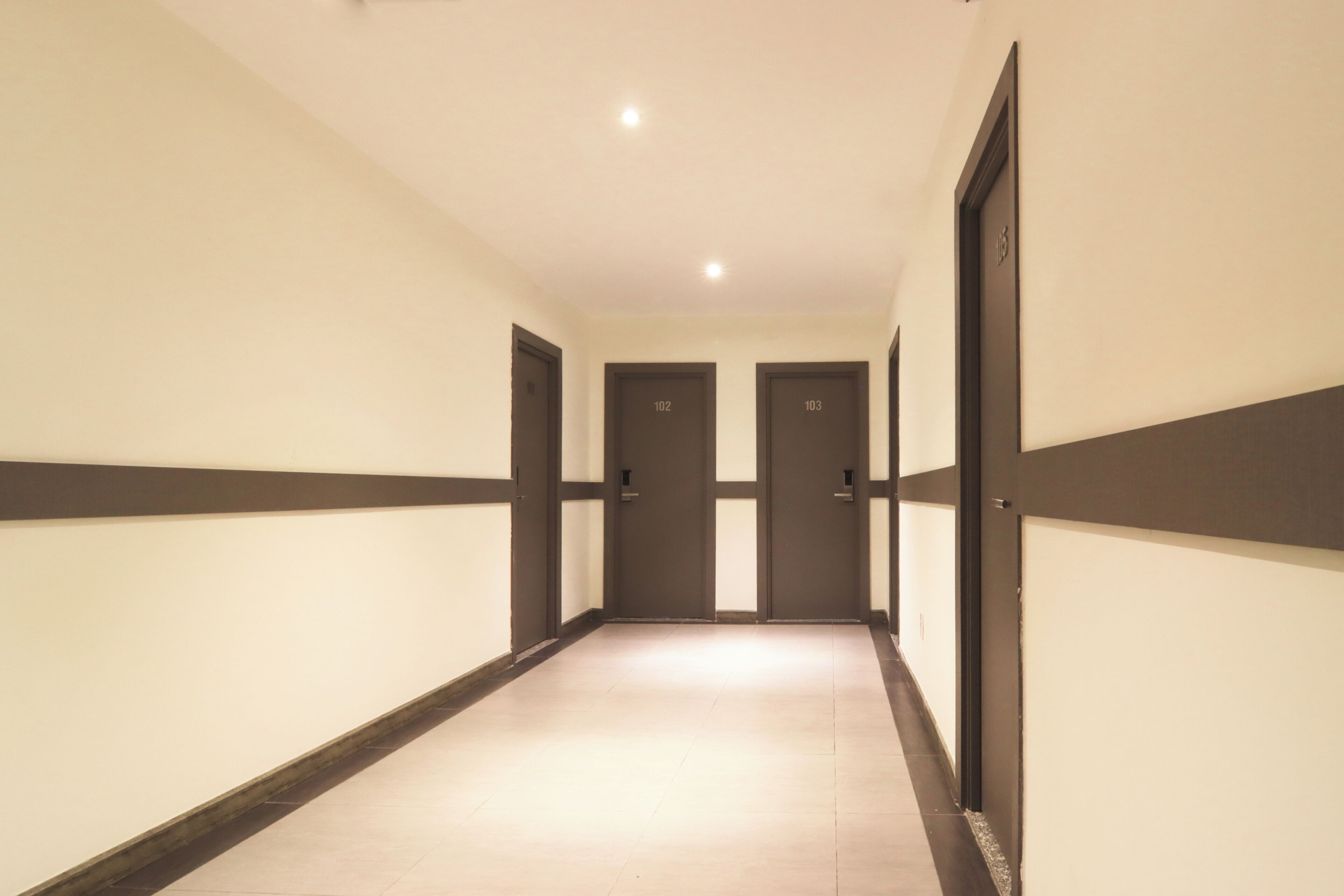 Corredor com portas numeradas 102 e 103, chão de azulejos e teto com iluminação embutida.