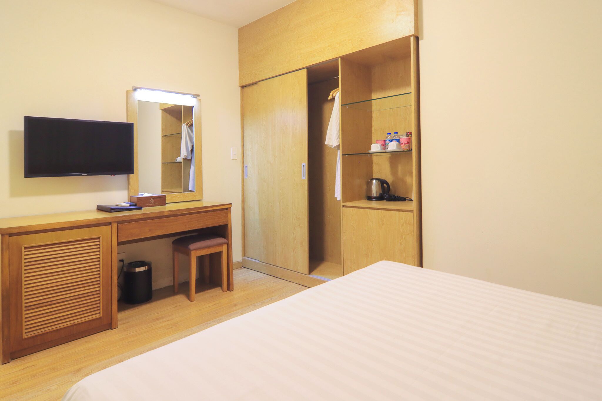 Una camera d'albergo con un letto, una scrivania con uno specchio, una televisione, un armadio e uno scaffale con articoli da toilette.