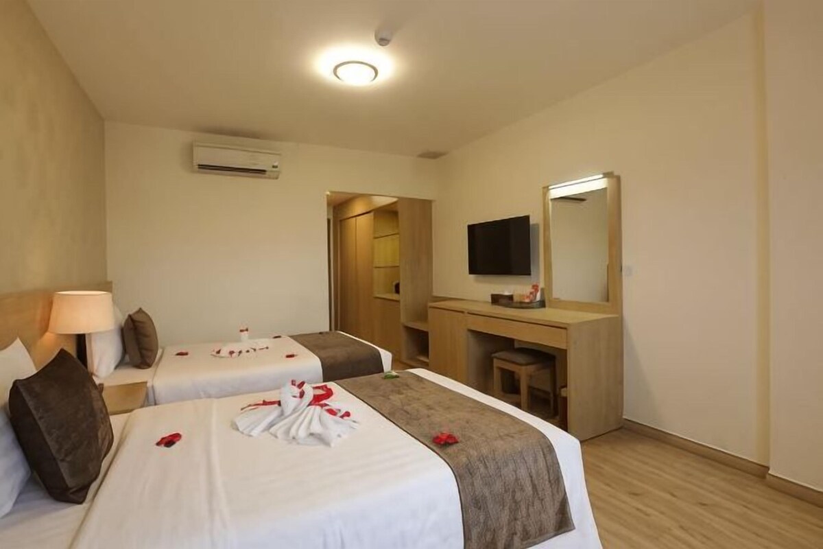 A hotel room with two beds, a desk, a TV, and a mirror.