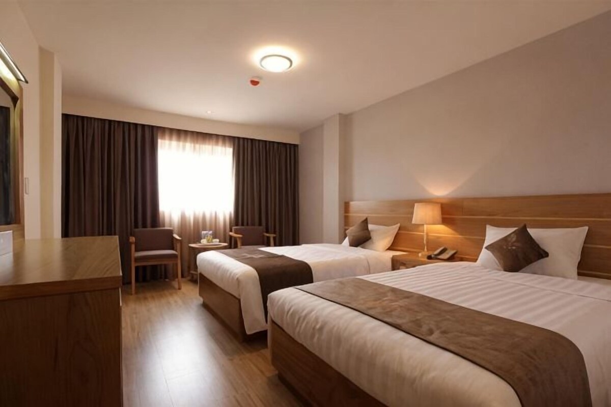 A hotel room with two beds, a desk, a chair, and a window with curtains.