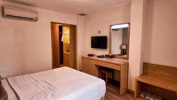 Une chambre d’hôtel avec un lit, un bureau en bois, un miroir, une télévision et un porte-chaussures.