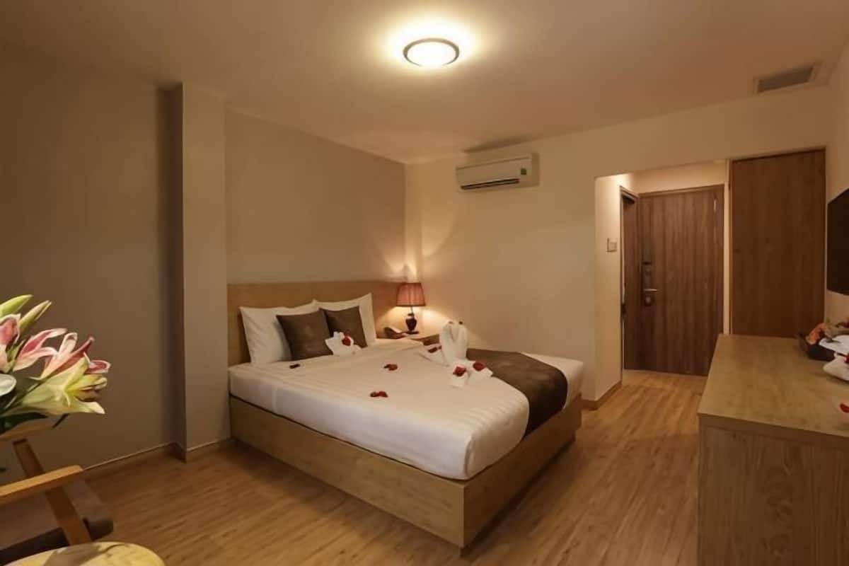 A hotel room with a bed, bedside table, lamp, and a wooden floor.