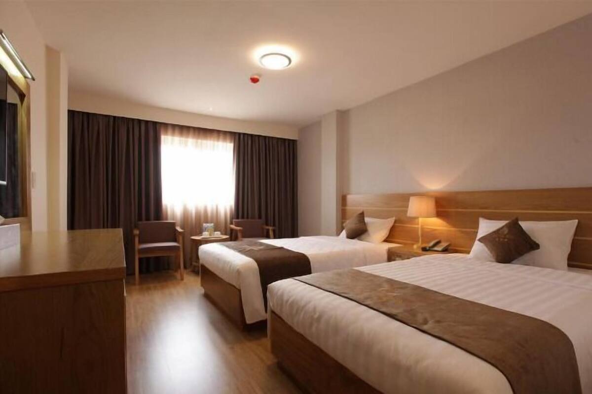 A hotel room with two beds, a desk, a chair, a TV, and a window with curtains.