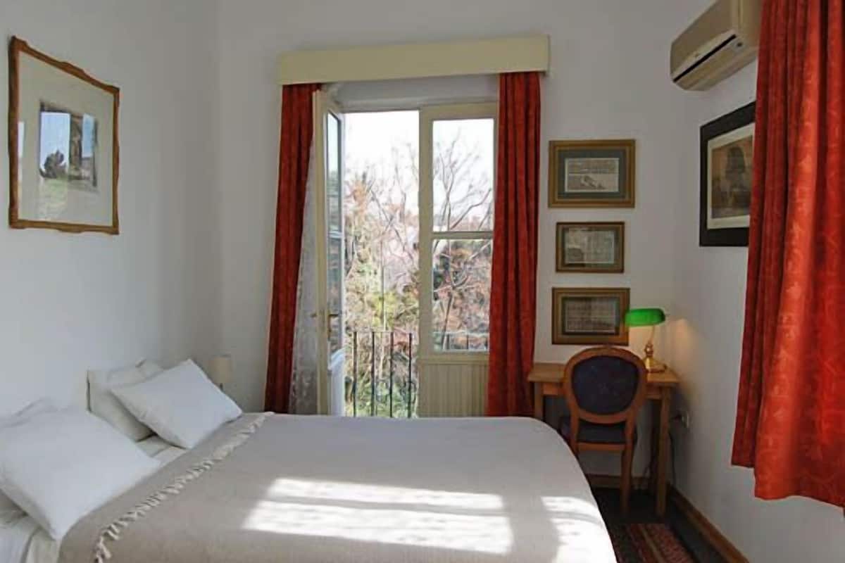 A bedroom with a bed, a desk, and a window with curtains.