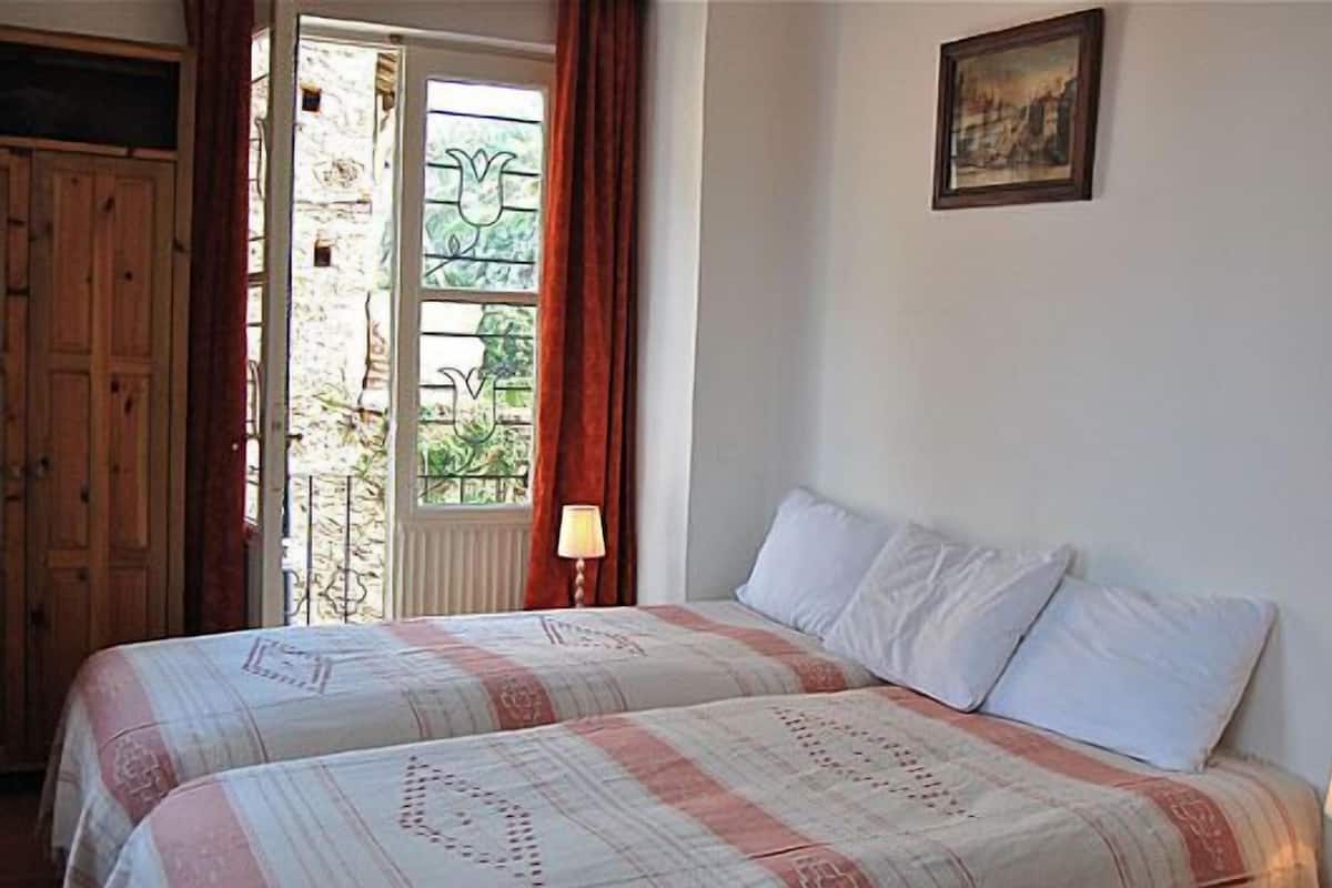 A bedroom with two beds, a window with curtains, a lamp, and a painting on the wall.