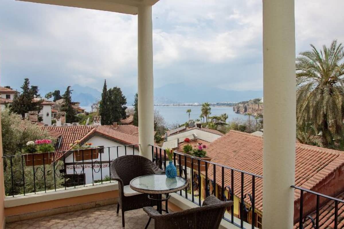 A balcony with a table and chairs, overlooking a coastal area with buildings and palm trees.
