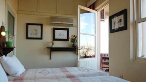 Un dormitorio con cama, estante con marcos de fotos, ventana y puerta que da a otra habitación.
