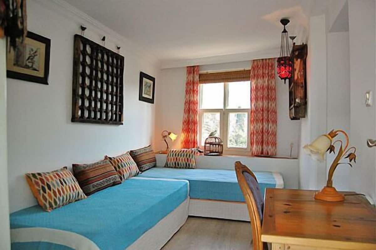 A room with two blue beds, a wooden table, and a window with curtains.