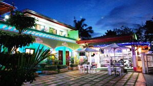 A courtyard with outdoor seating, a covered area, and a building with colorful lighting. - DZR Guest House (Puerto Princesa)