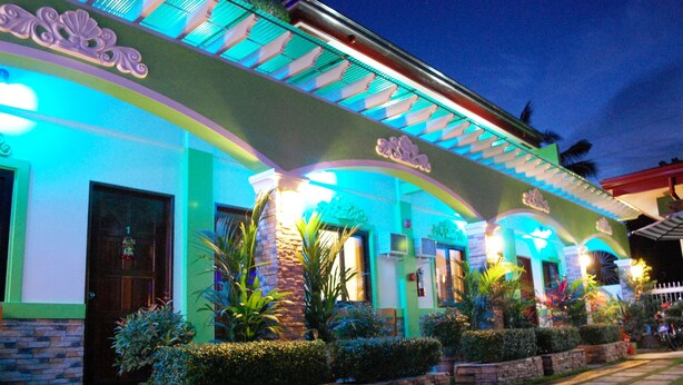 A building with a green facade, multiple doors, and a tiled walkway. - DZR Guest House (Puerto Princesa)