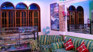 A modern lounge area with a curved ceiling, seating with patterned upholstery, a glass coffee table, and a decorative plant. - DZR Guest House (Puerto Princesa)