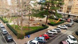 A parking area with multiple cars, a playground, and a building in the background. - LovelyBed (Aprilia)