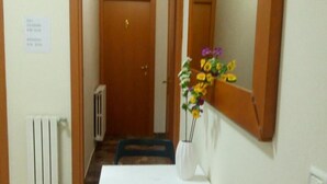 A hallway with a white table and black chairs, a radiator, and a door at the end. - LovelyBed (Aprilia)