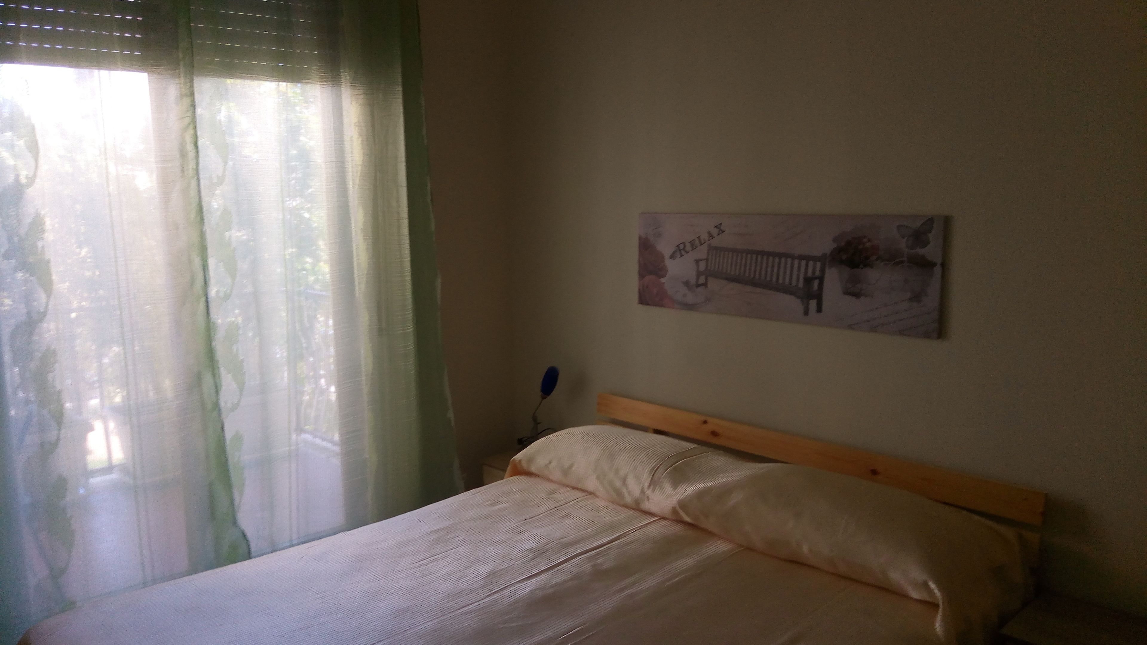 Ein Schlafzimmer mit einem Bett, einem Nachttisch, einer Wandlampe und einem Poster.