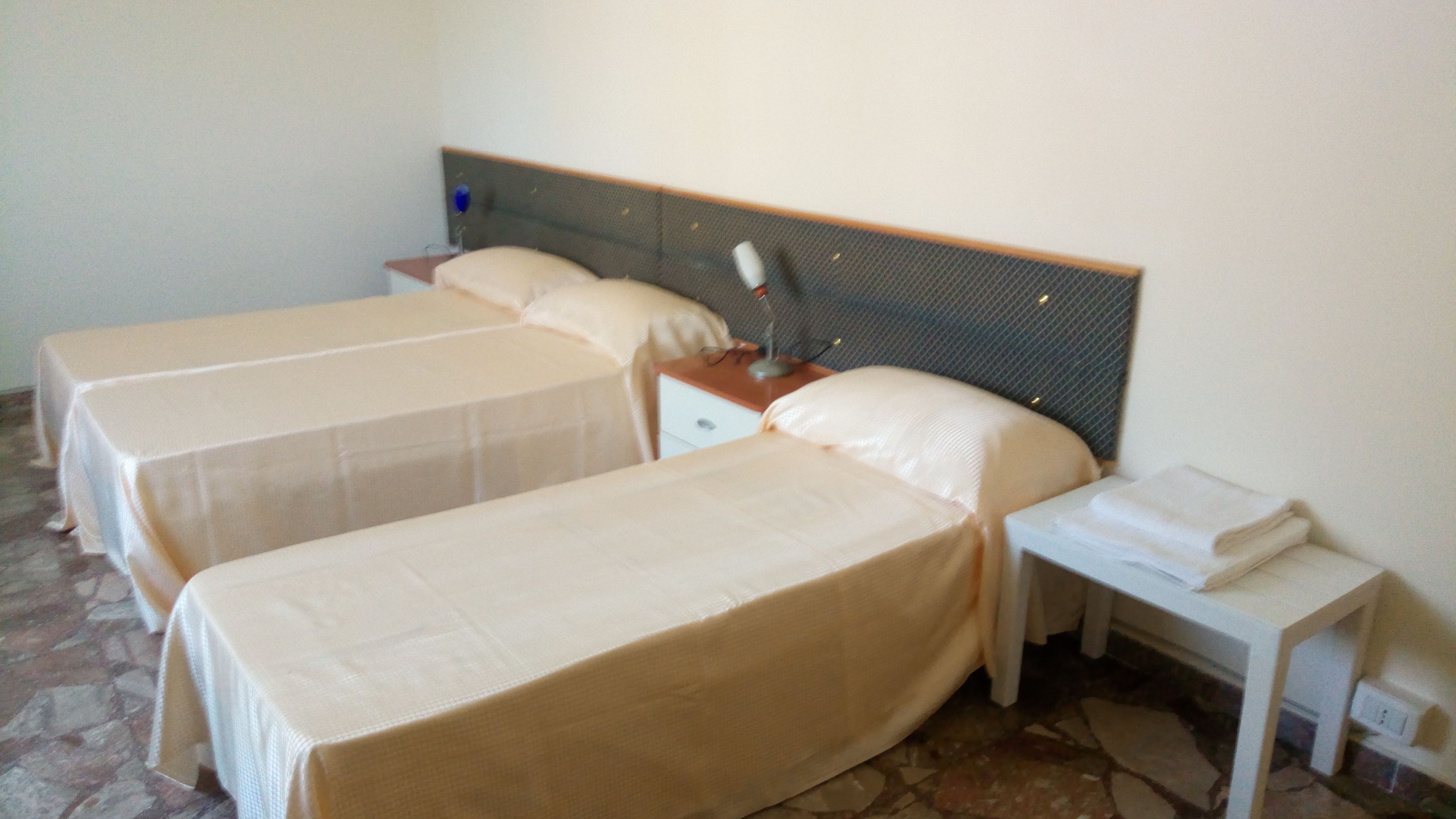 A hotel room with two single beds, a bedside table with a lamp, and a small nightstand.