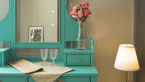 A teal vanity with a mirror, a vase with pink flowers, and a lamp on a wooden side table. - Heyha Hotel (Bangkok)