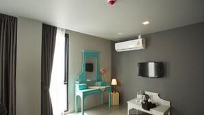 A modern hotel room with a teal vanity, a white bench, a flat-screen TV, and a mounted air conditioner. - Heyha Hotel (Bangkok)