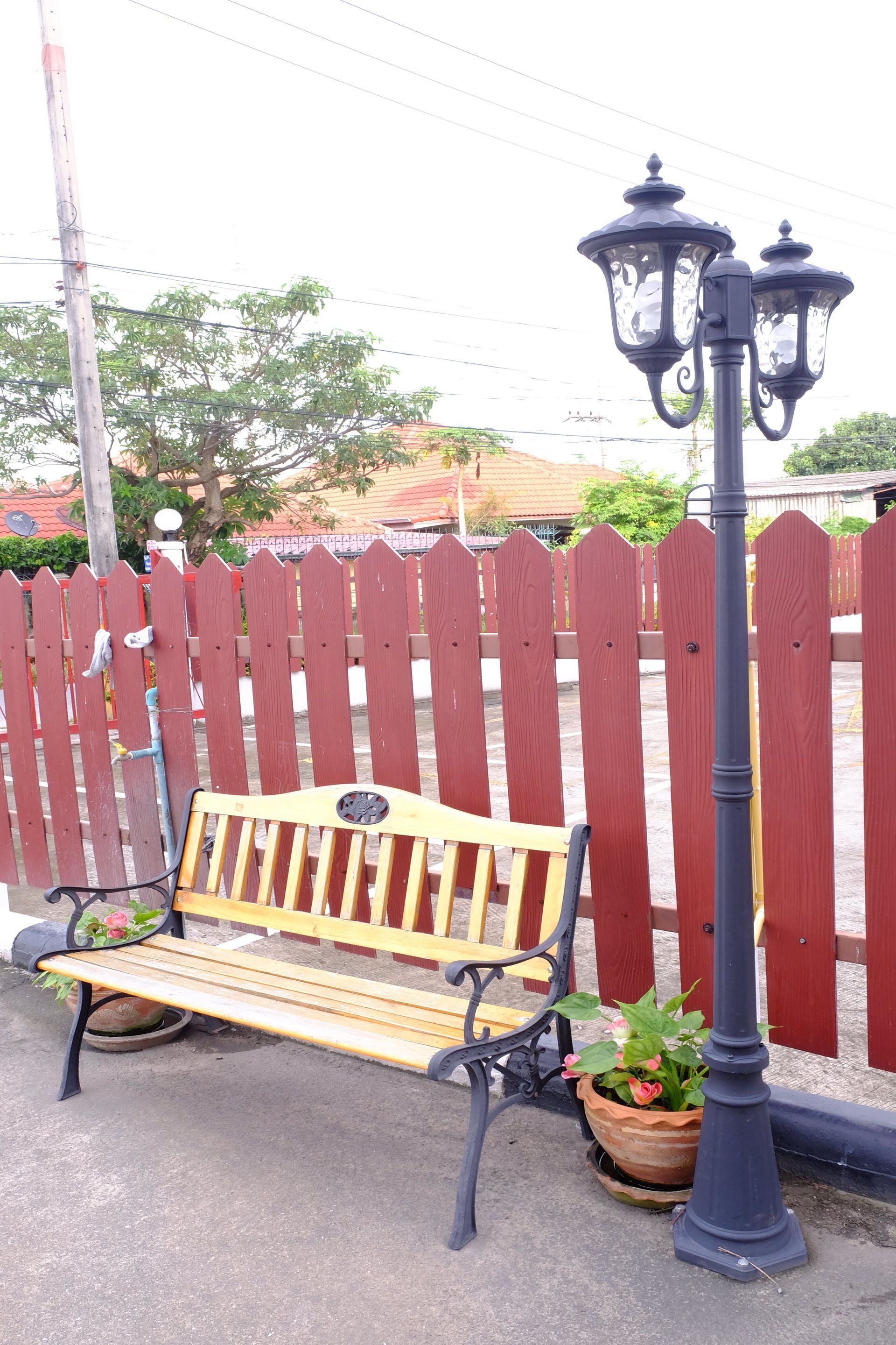 A wooden bench with a metal frame, a potted plant, and a black street lamp.