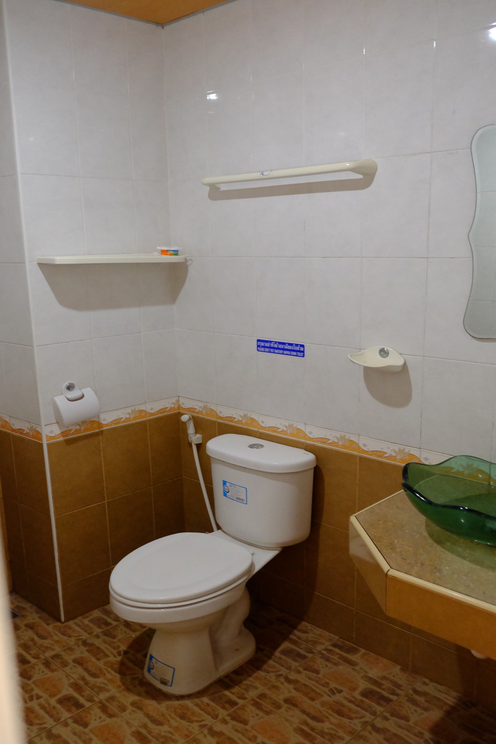 Een kleine badkamer met een toilet, een wastafel met een groene wasbak en een plank boven het toilet.