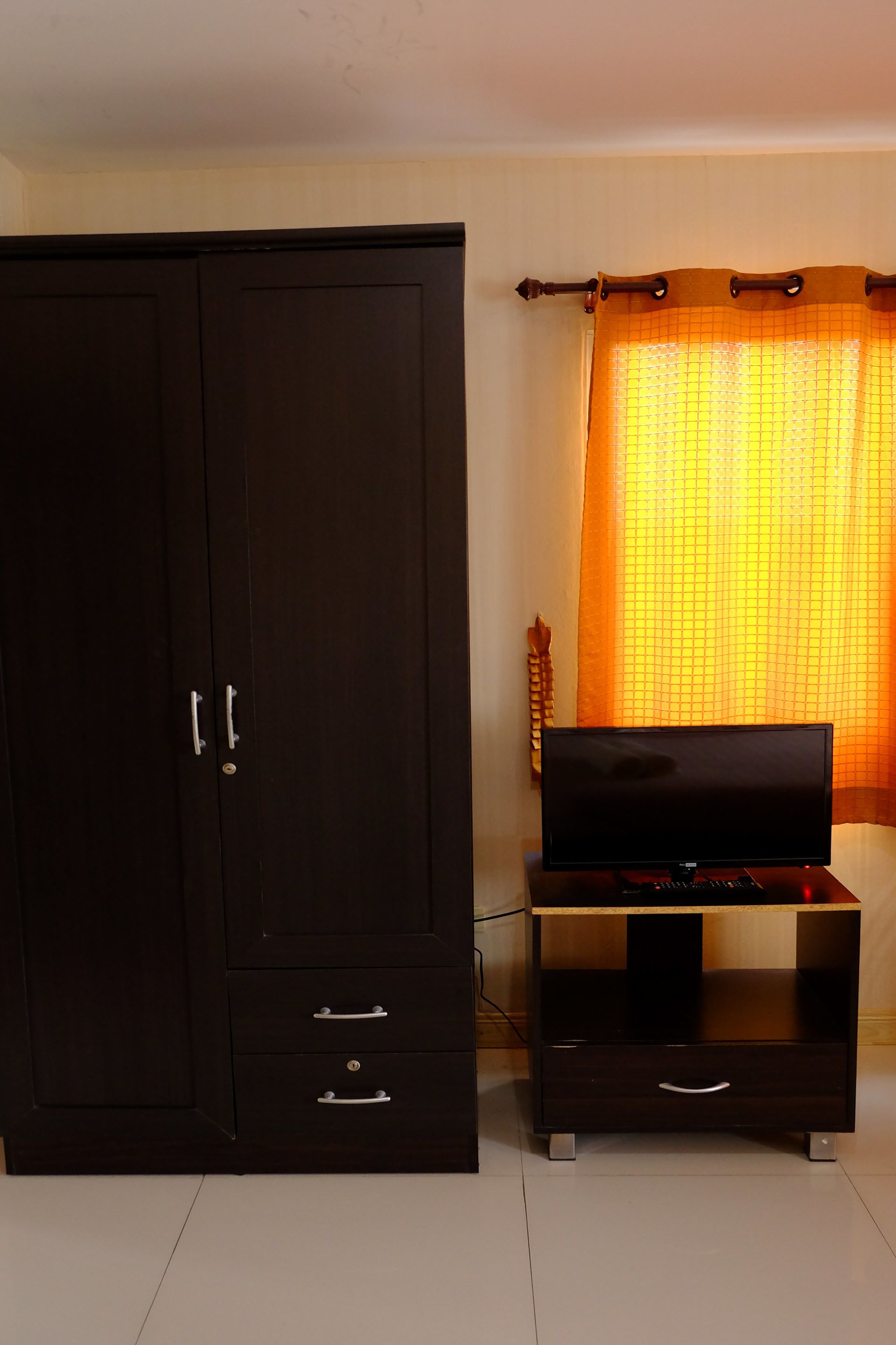 Una habitación con un armario de madera oscura, un mueble bajo para televisión de madera y una cortina.