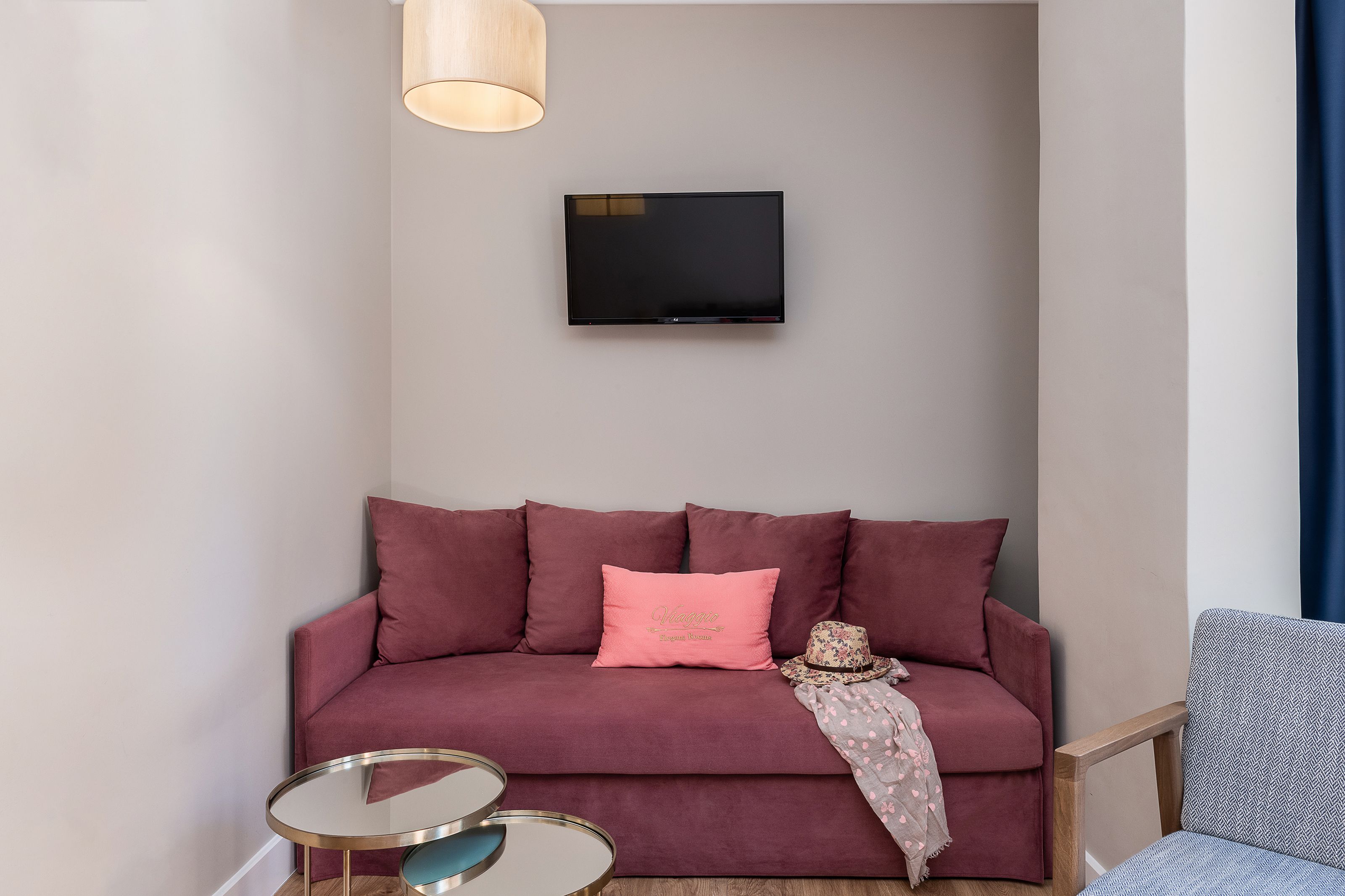 Un salon avec un canapé rouge, un coussin rose, une petite table ronde et un téléviseur fixé au mur.
