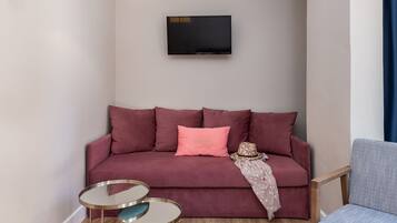 Un salon avec un canapé rouge, un coussin rose, une petite table ronde et un téléviseur fixé au mur.