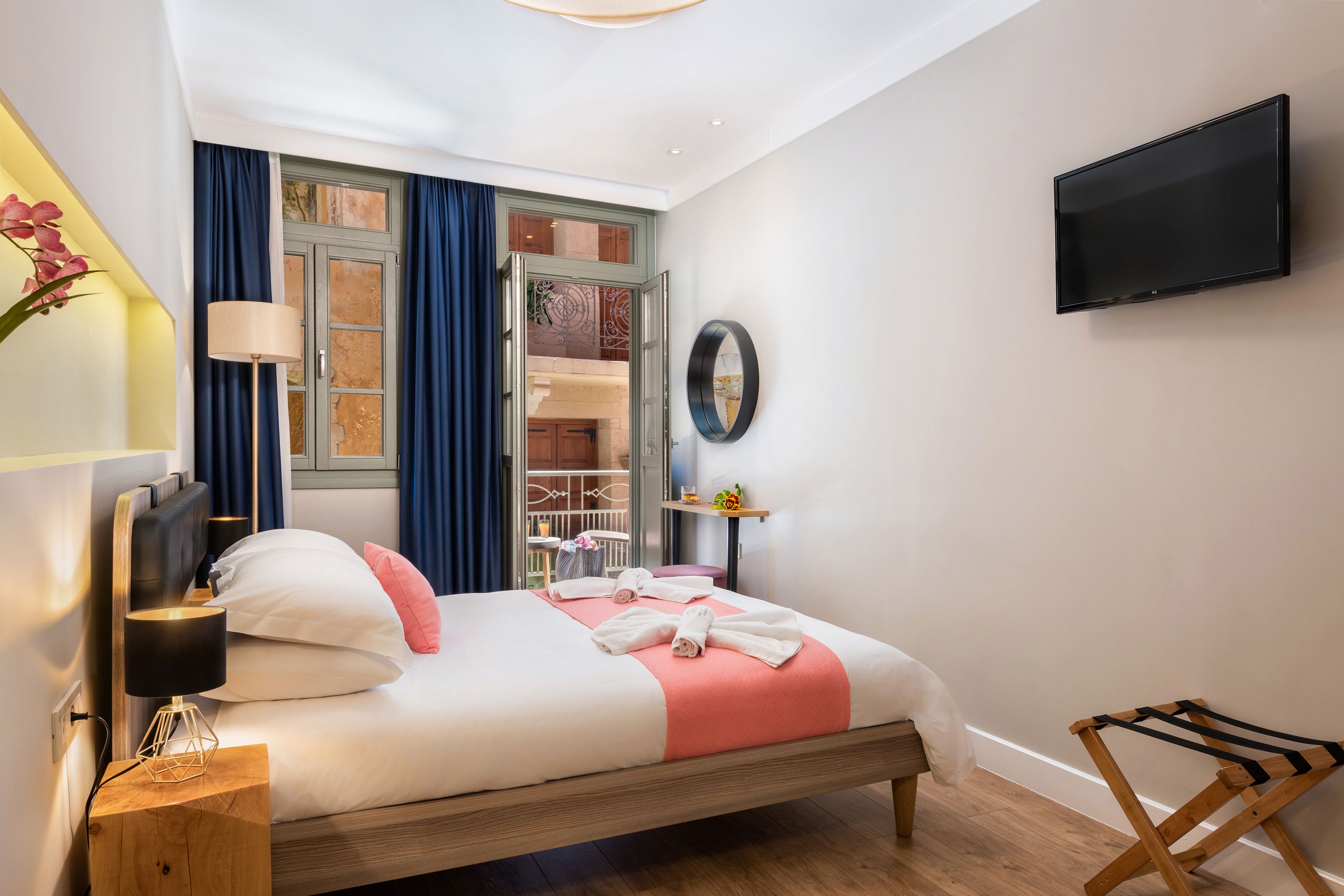 Una habitación de hotel moderna con una cama, un televisor montado en la pared y un balcón con vistas.