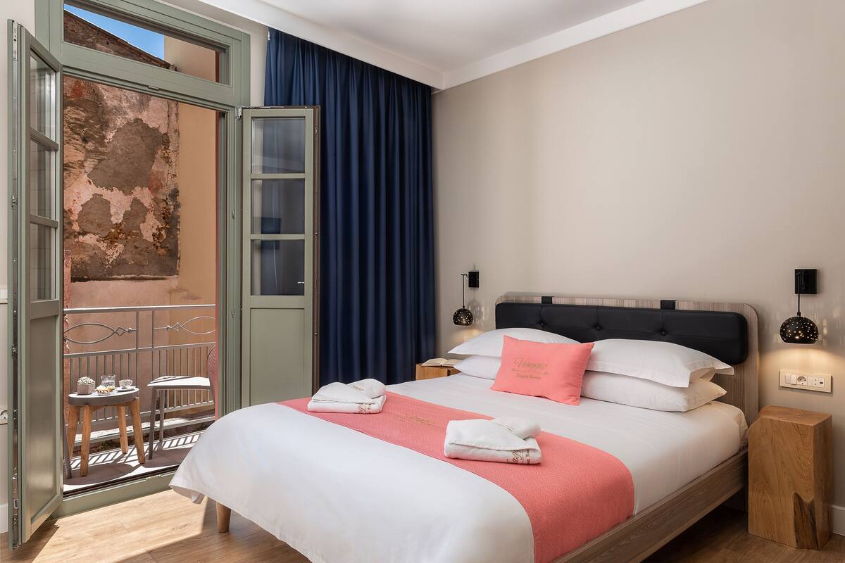 Une chambre à coucher comprenant un lit, une table de chevet, une lampe de chevet, une fenêtre avec des rideaux et un balcon avec une table et des chaises.