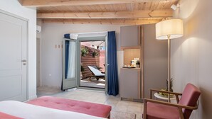 A bedroom with a bed, a chair, a desk, and a door leading to an outdoor area with a table and chairs. - Viaggio Elegant Rooms (Chania)