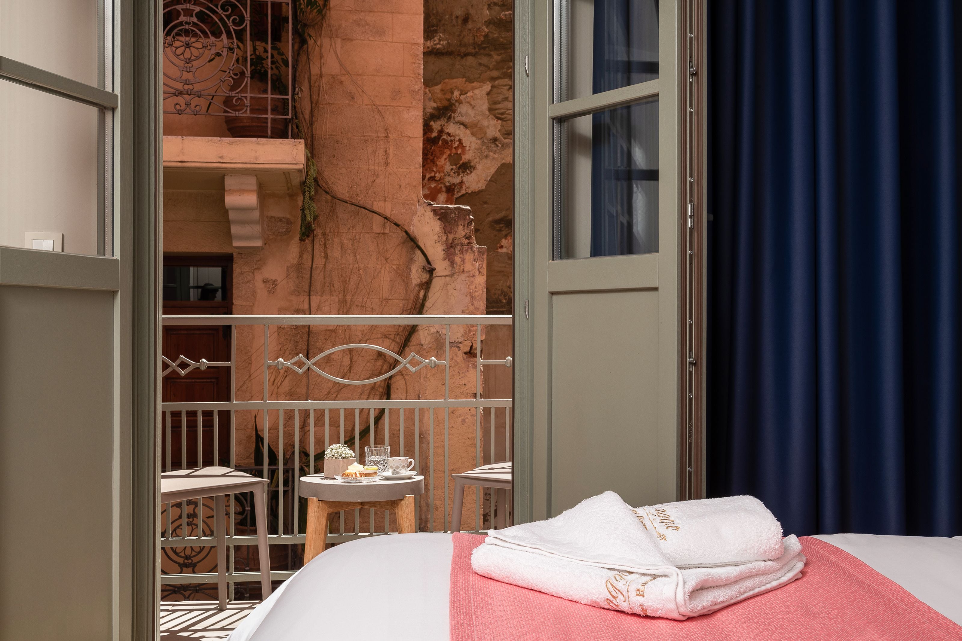 A hotel room with a bed, a small table with a cup and a glass, and a balcony with a railing.