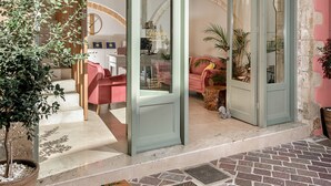 A hotel entrance with a stone archway, a potted plant, and a red sofa inside. - Viaggio Elegant Rooms (Chania)